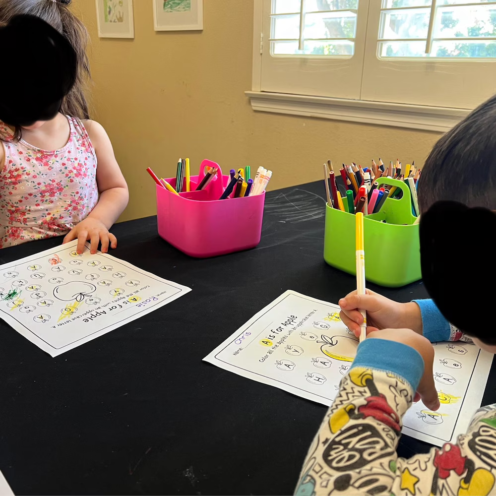 Two children working on worksheets at table with caddies