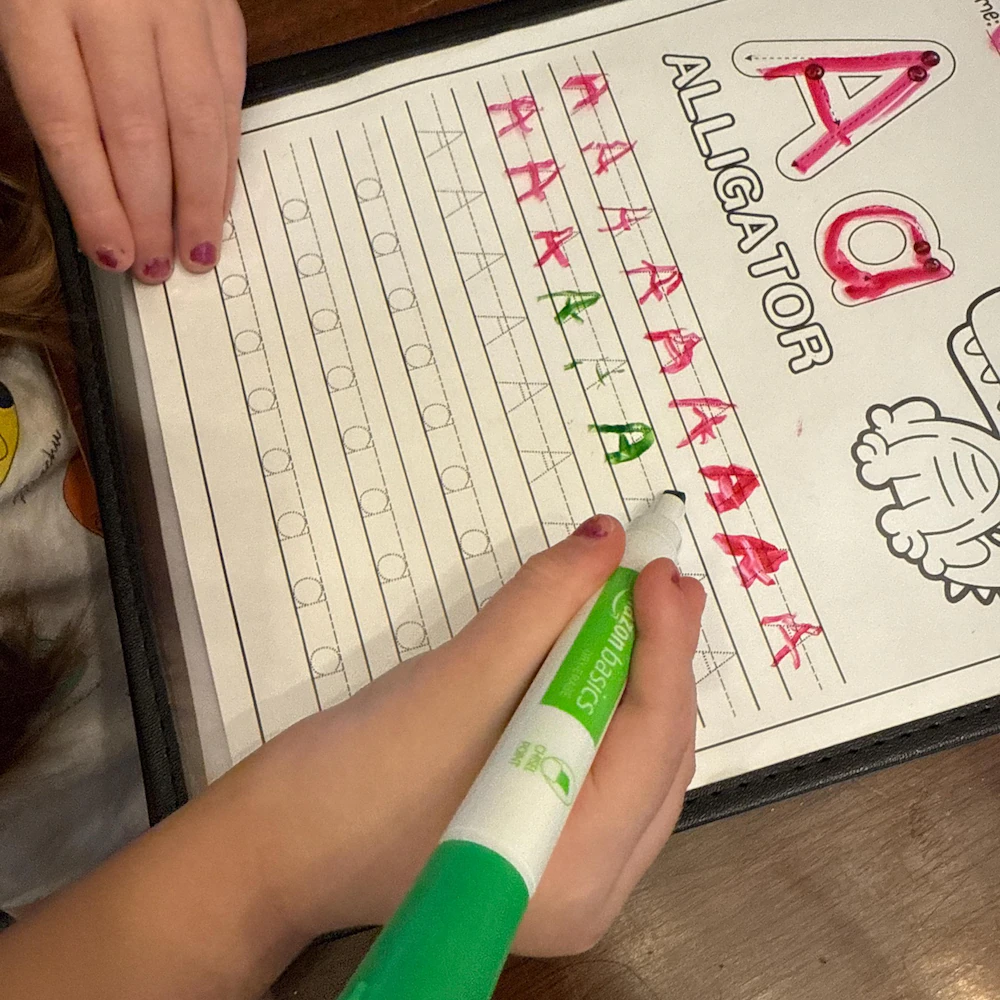 Hands practicing letter tracing with green marker